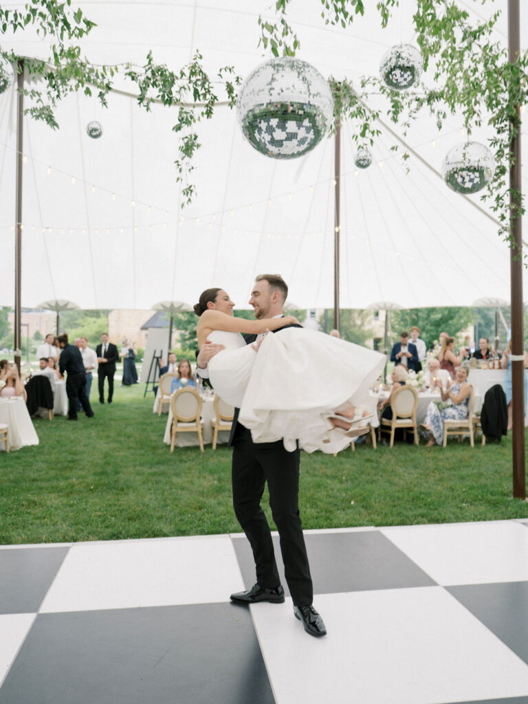 Groom lifts bride on the dance floor surrounded by guests under hanging disco balls at Saint Mary’s Notre Dame wedding – Cynthia Mae Photo.