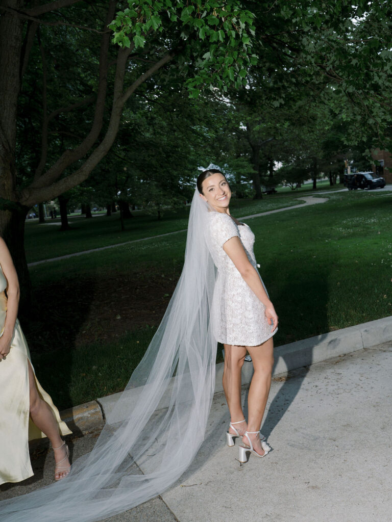 Bride in short sparkly reception dress with cathedral-length veil, smiling before rejoining the dance floor – Cynthia Mae Photo.