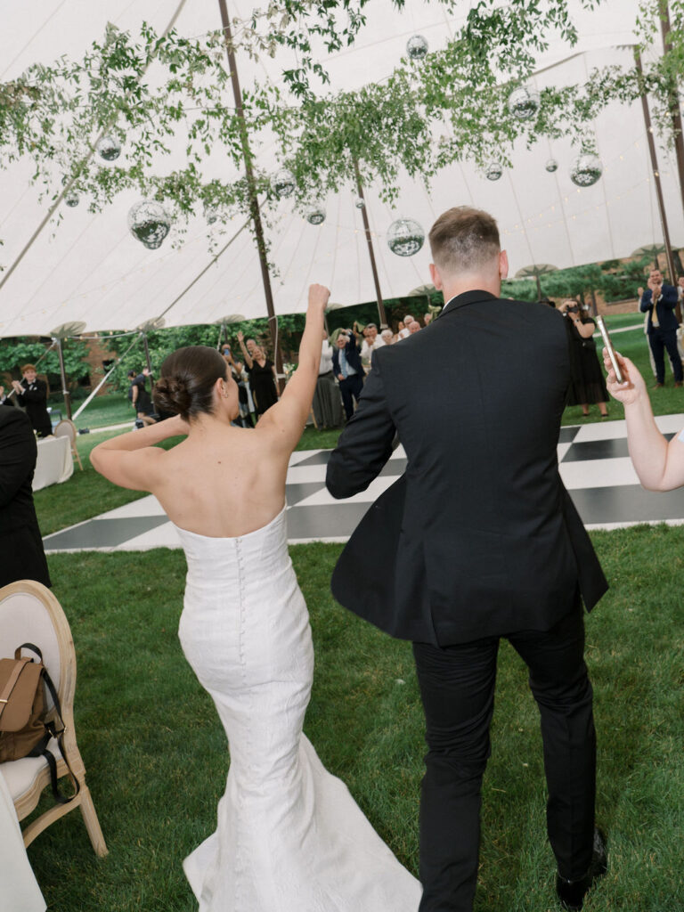 Bride and groom enter their tented reception to cheers, dancing across black-and-white dance floor – Cynthia Mae Photo.
