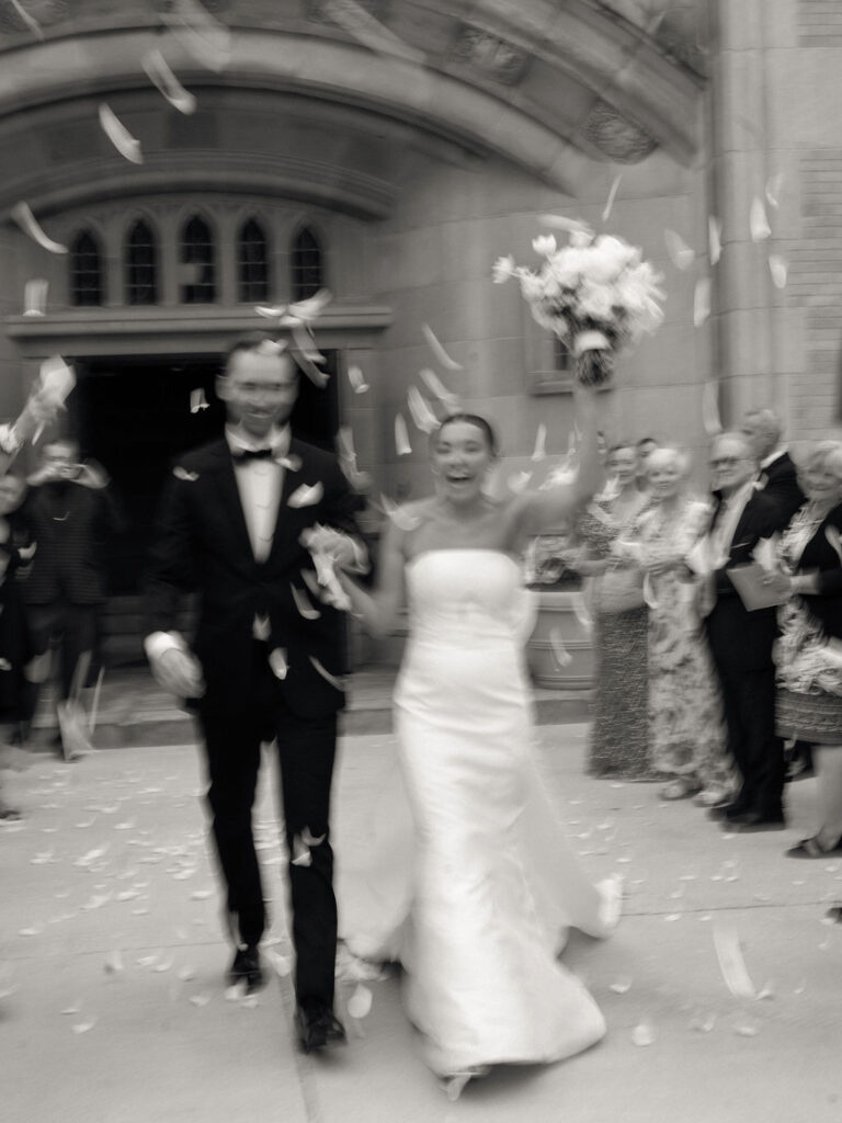 Motion-blurred photo of bride and groom celebrating during petal toss exit outside Church of Our Lady of Loretto at Saint Mary’s College – Cynthia Mae Photo.