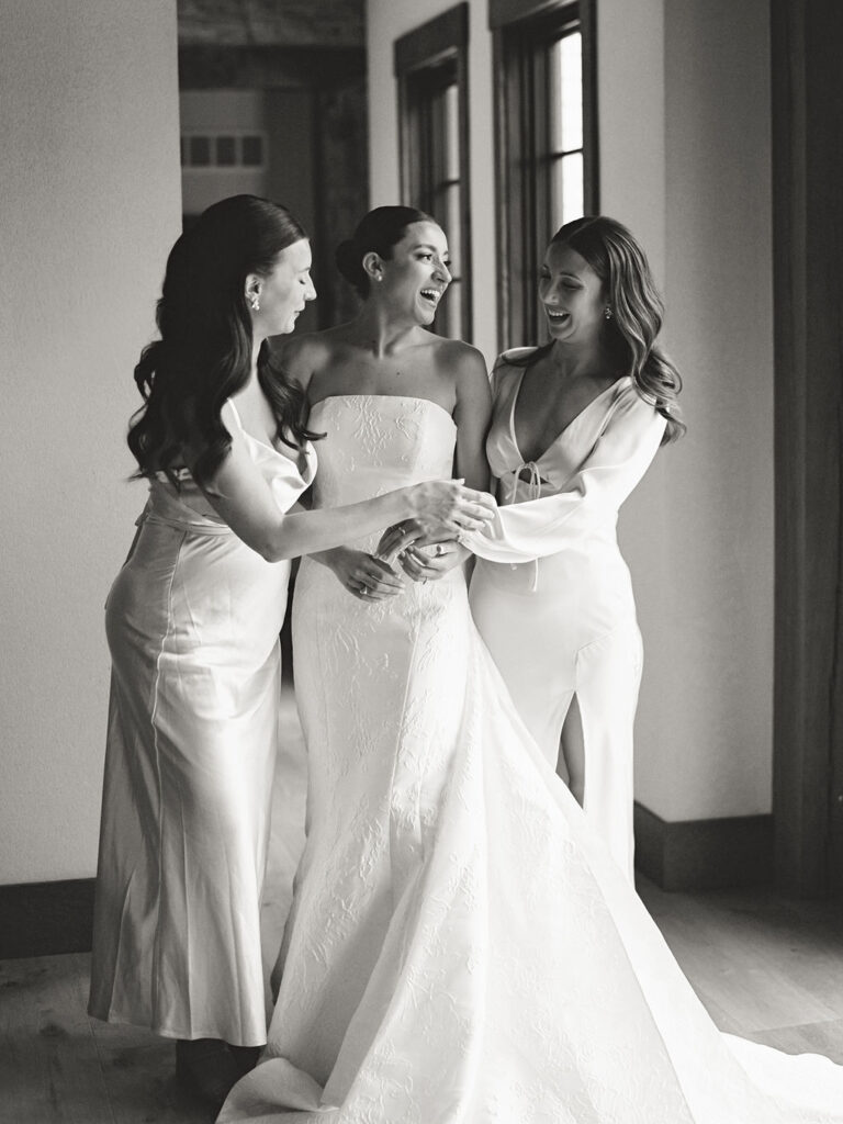 Bride laughing with her bridesmaids in natural light hallway before Saint Mary’s Notre Dame wedding – film photograph by Cynthia Mae Photo.