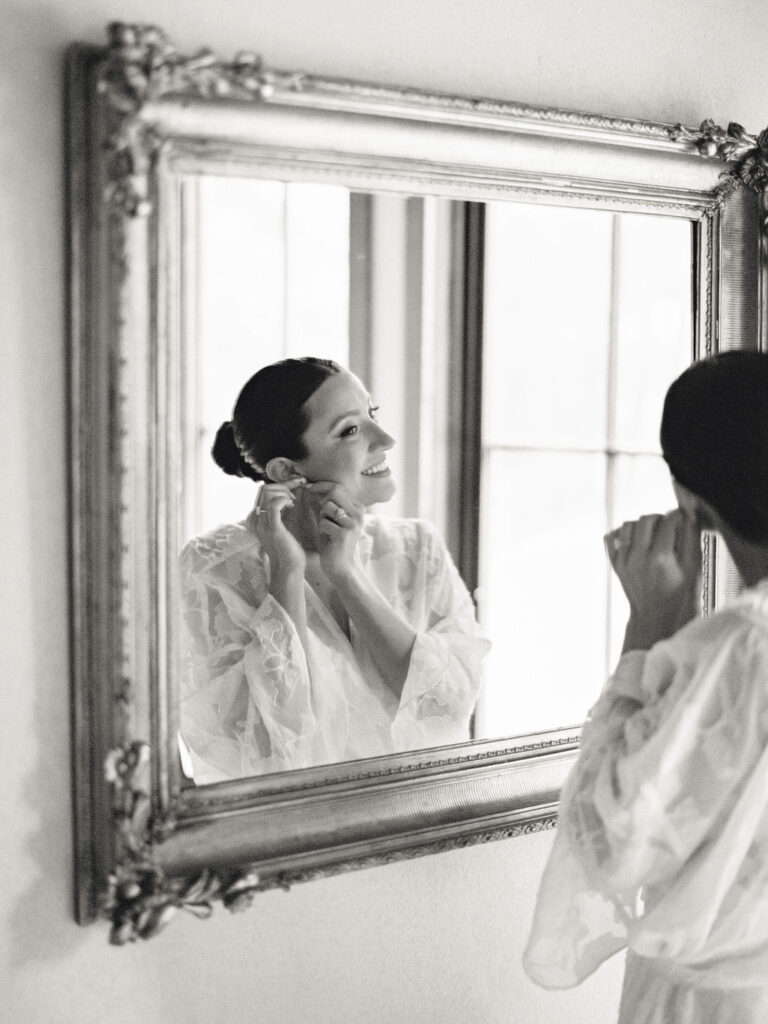 Black and white film photo of a bride putting her earrings in