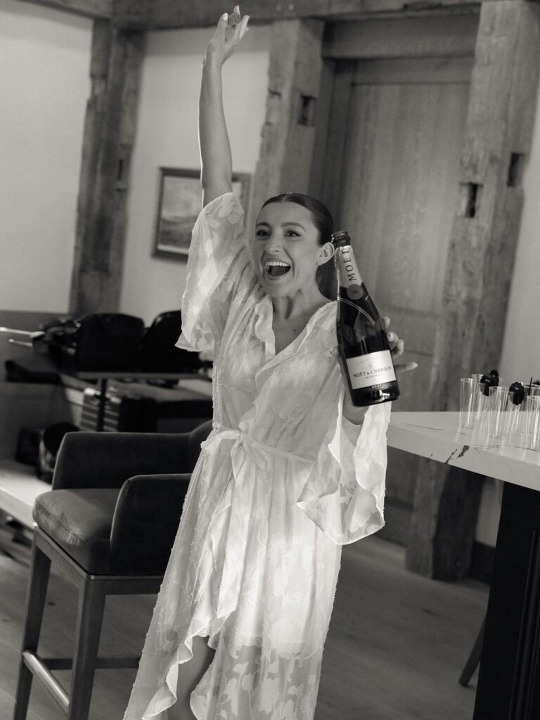Bride in white robe celebrating with champagne during Saint Mary’s Notre Dame wedding morning – film photograph by Cynthia Mae Photo.