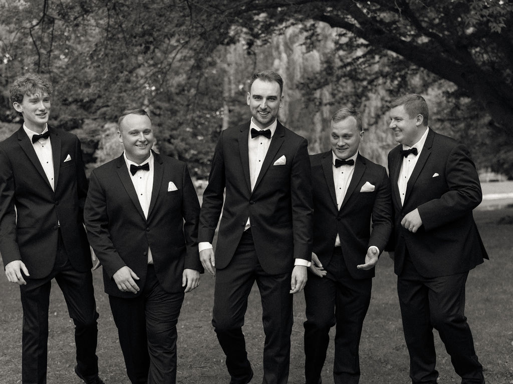 Black and white photo of groom and groomsmen walking and laughing before Saint Mary’s Notre Dame wedding – Cynthia Mae Photo.