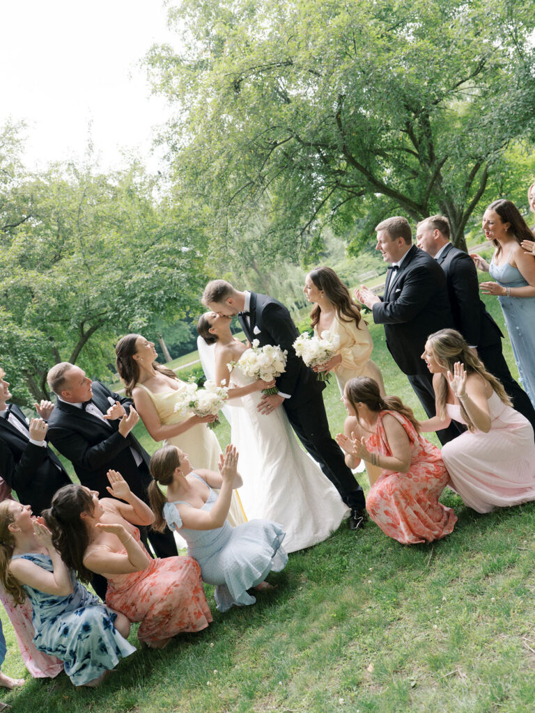 Bride and groom kissing surrounded by their wedding party in colorful summer attire at Saint Mary’s College – Cynthia Mae Photo.