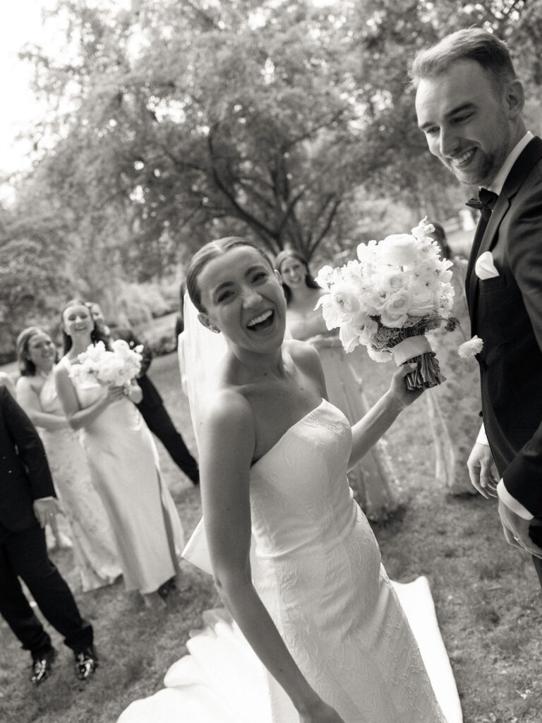 Black and white candid photo of a bride and groom smiling during their wedding party photos