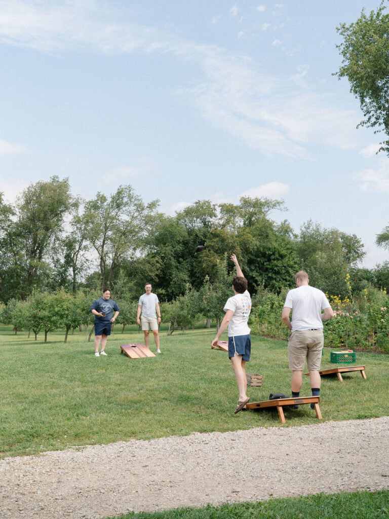 Groomsmen playing cornhole before an Of The Land wedding ceremony.