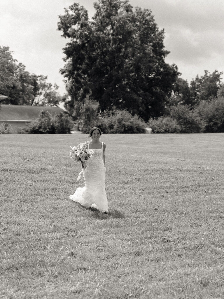Black and white photo of the bride walking out to the gardens to share a first look with her groom.