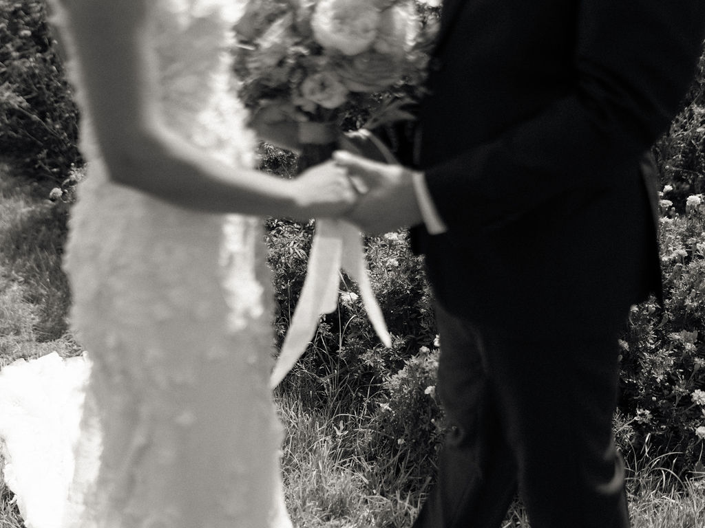 Black and white close-up of couple holding hands during first look at an Of The Land wedding.