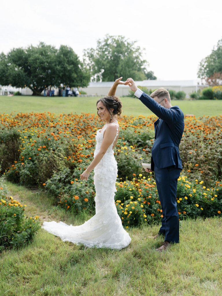 Groom twirling his bride during their first look at Of The Land wedding venue in the gardens. 