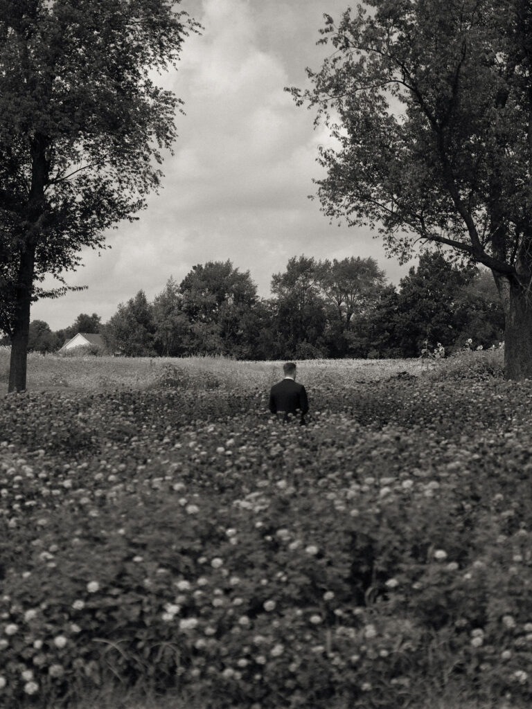 Black and white photo of the groom waiting in the gardens for his first look.