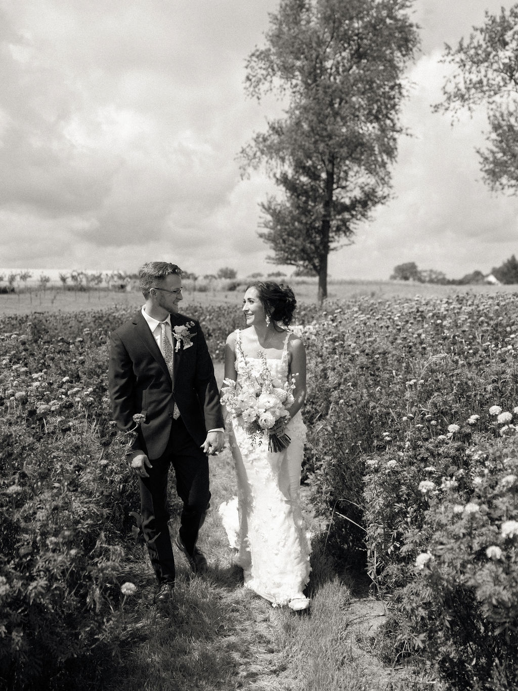Black and white photo of a bride and groom walking through the gardens at Of The Land wedding venue in Marshall, Michigan.