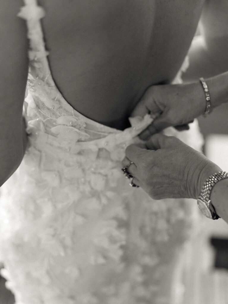Close up black and white photo of the bride getting her dress buttoned up.