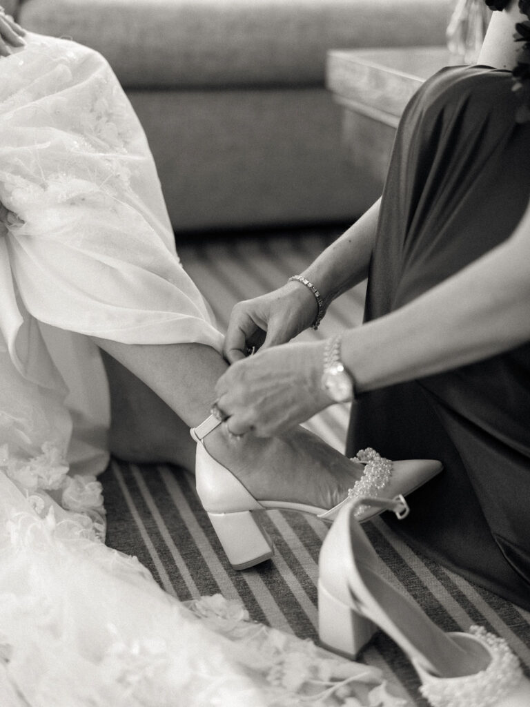 Black and white photo of the bride getting her shoes put on.