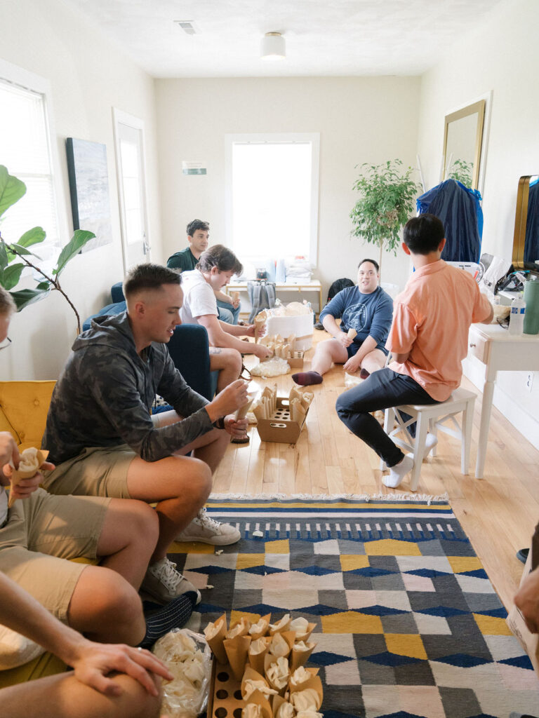Group of groomsmen preparing petal toss cones during getting ready time at an Of The Land wedding.