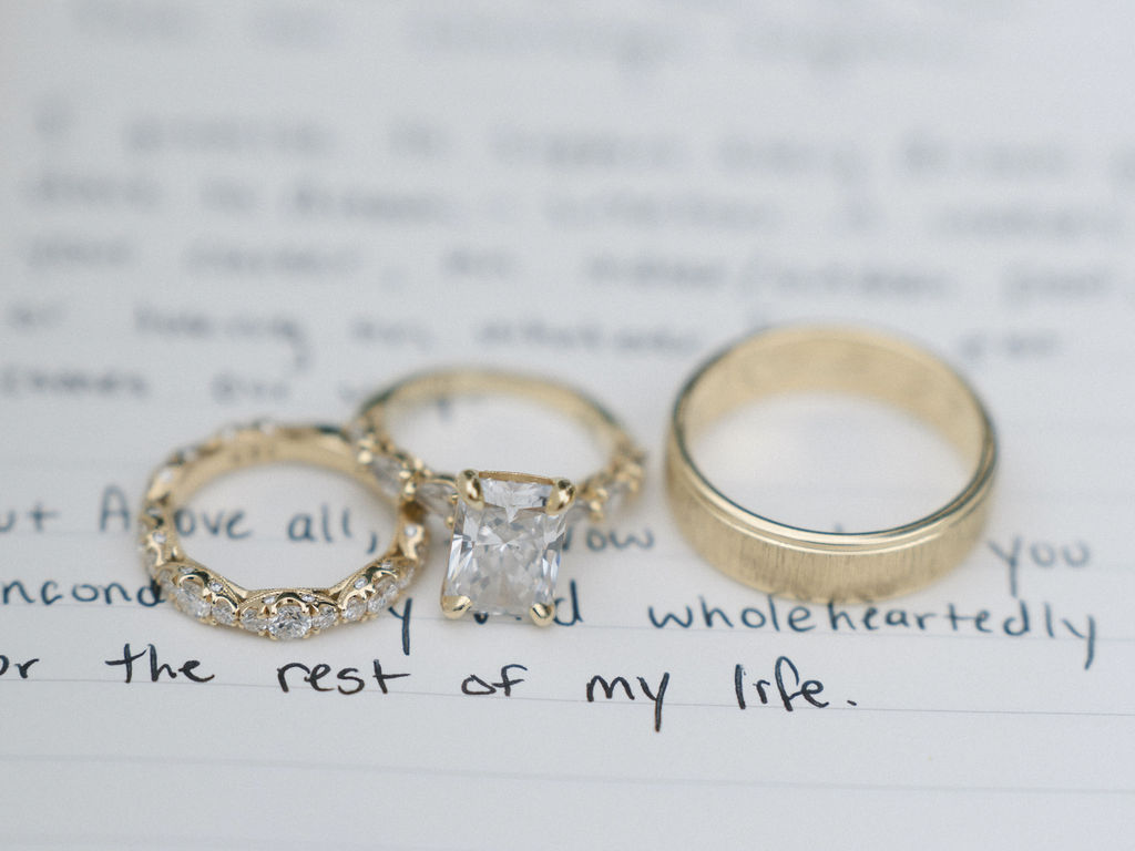 Close up detail shot of the brides rings and grooms band over handwritten vows.