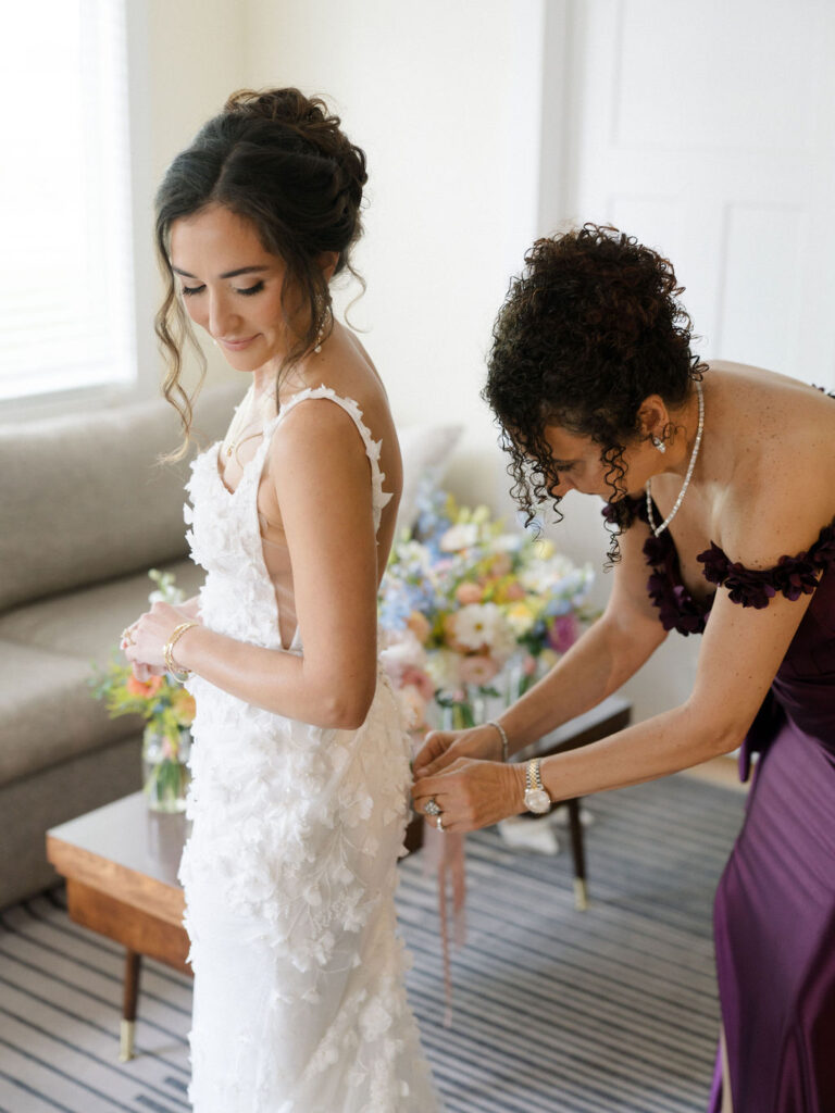 Bride getting buttoned into floral-textured wedding gown inside the Farm Flat at an Of The Land wedding