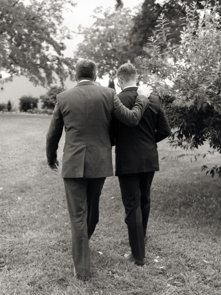Black and white candid wedding photo of the groom walking with his father.