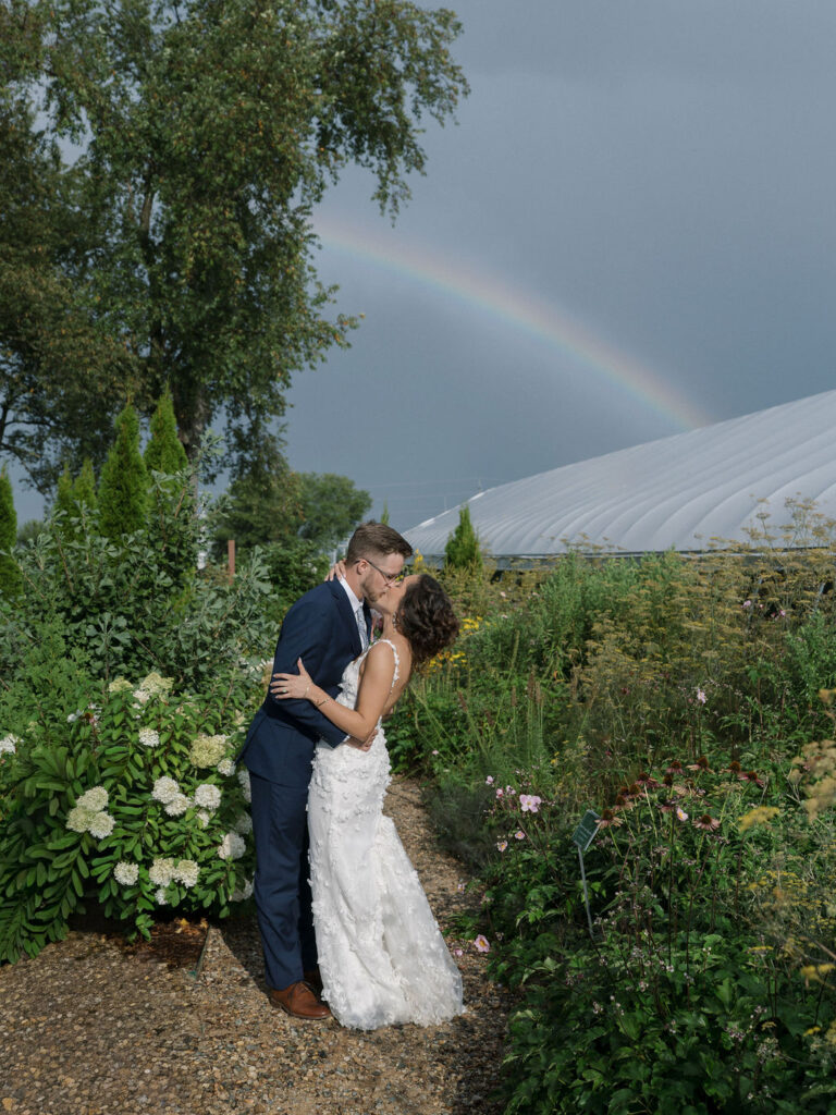 Bride and groom kissing with a rainbow in the background for their Of The Land wedding reception in Marshall, Michigan