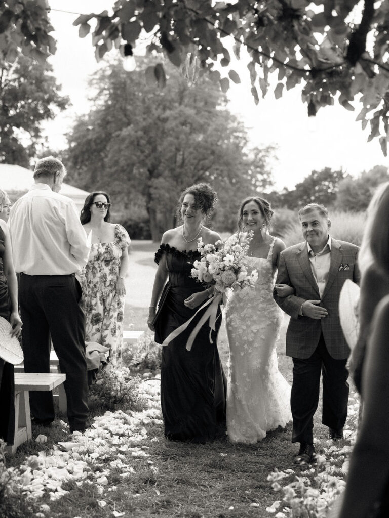 Bride walking down a petal-lined aisle toward the Mulberry tree ceremony space.