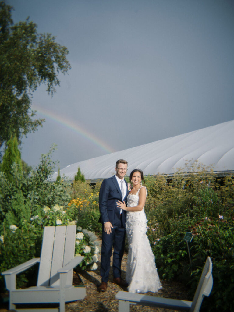 Couple standing in the garden with a rainbow in the background at Of The Land wedding.