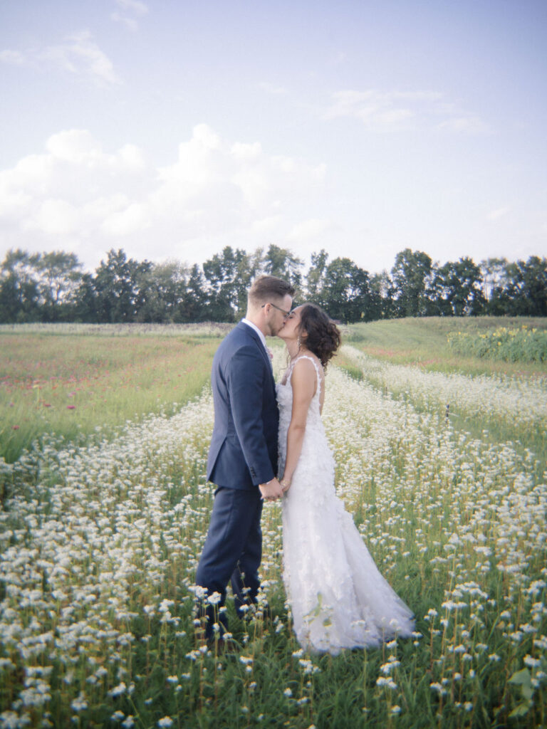 Couple standing in a field of small white blooms at sunset.