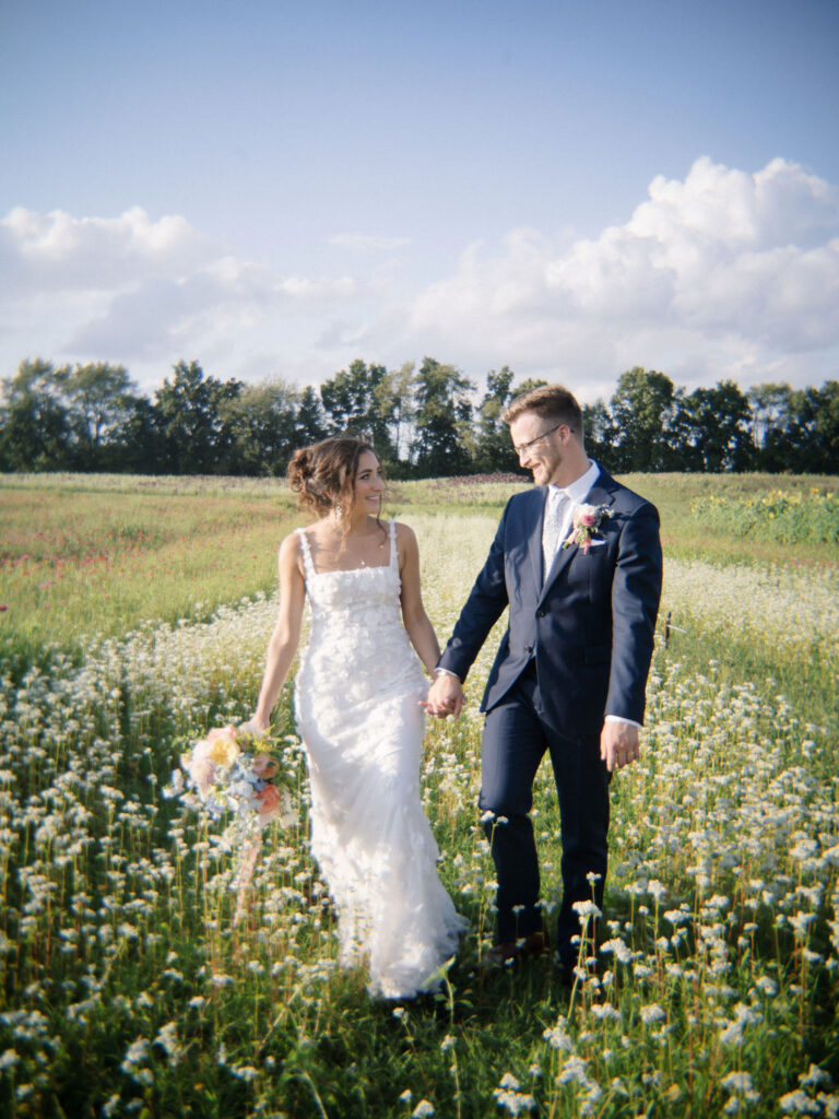 Couple walking hand-in-hand through wildflower rows at sunset.