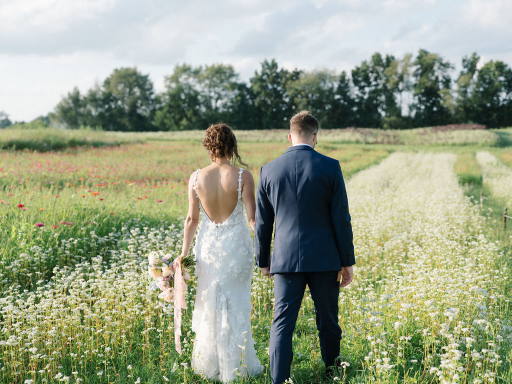 Bride and groom walking through the meadows at Of The Land wedding venue in Michigan.