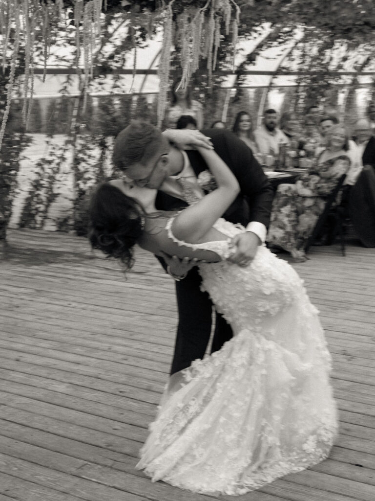 The groom dips the bride during their first dance inside the greenhouse at their Of The Land wedding, captured with a soft motion blur.