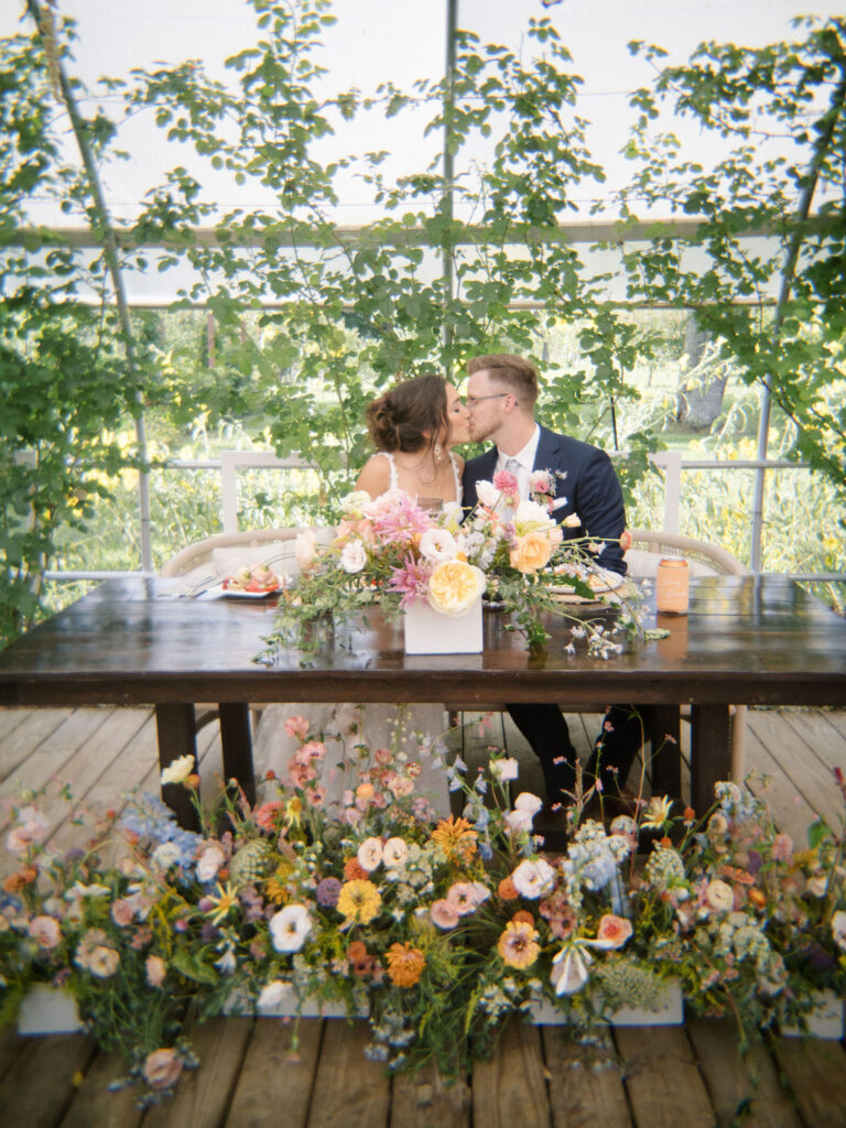 Bride and groom kissing at their sweethearts table at their Of The Land wedding reception in Michigan.