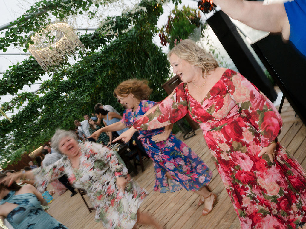 Guests dancing joyfully beneath hanging vines and warm lights during an Of The Land wedding reception.