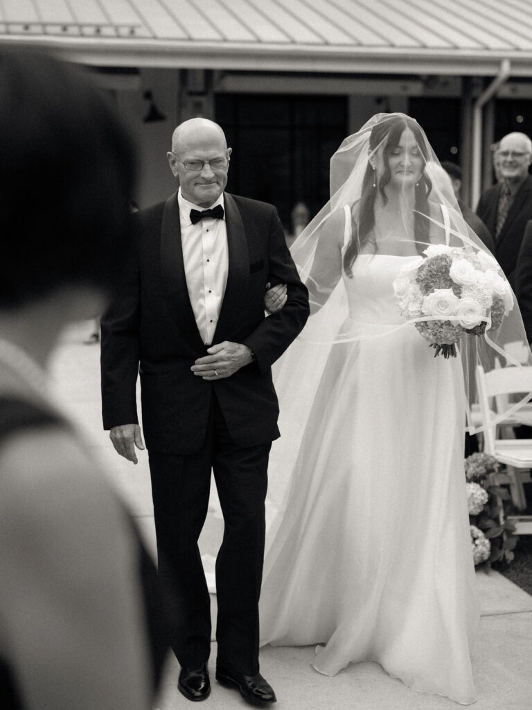 Black and white photo of a bride walking down the aisle with her father.