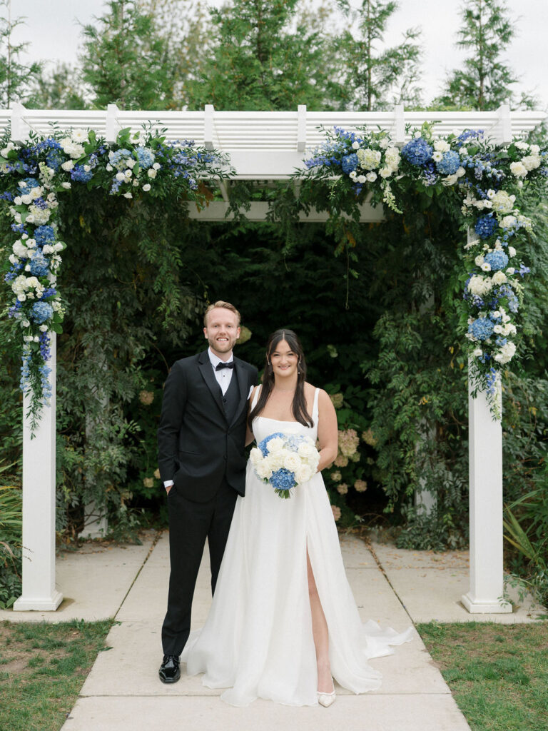 Bride and groom standing together beneath the floral ceremony pergola at Bay Pointe Woods.