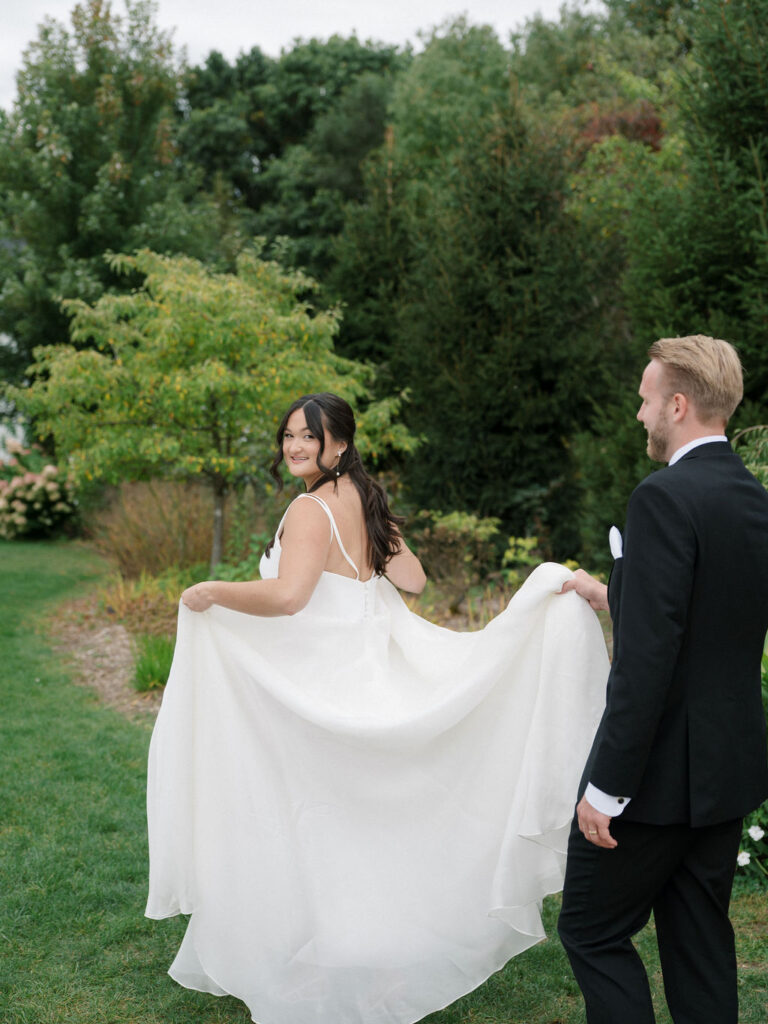 Bride walking and holding her dress while the groom holds the train during portraits at Bay Pointe Woods.