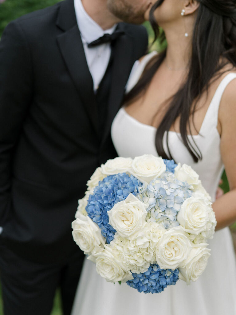Close-up of the bride and groom kissing with blue and white bouquet in the foreground.