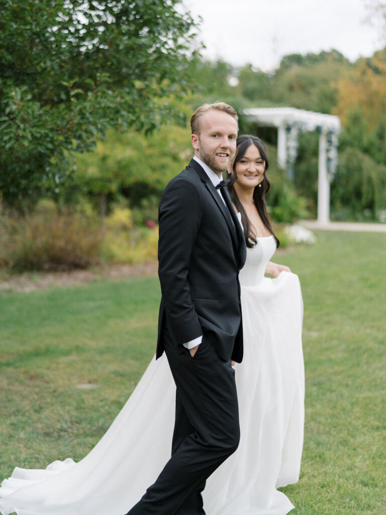 Side photo of a bride and groom walking across the lawn at Bay Pointe Woods.