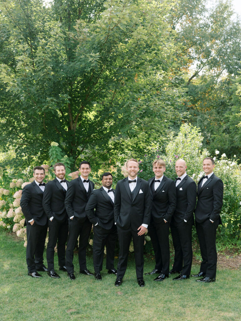Groomsmen standing together in black tuxes for wedding party photos at Bay Pointe Woods.
