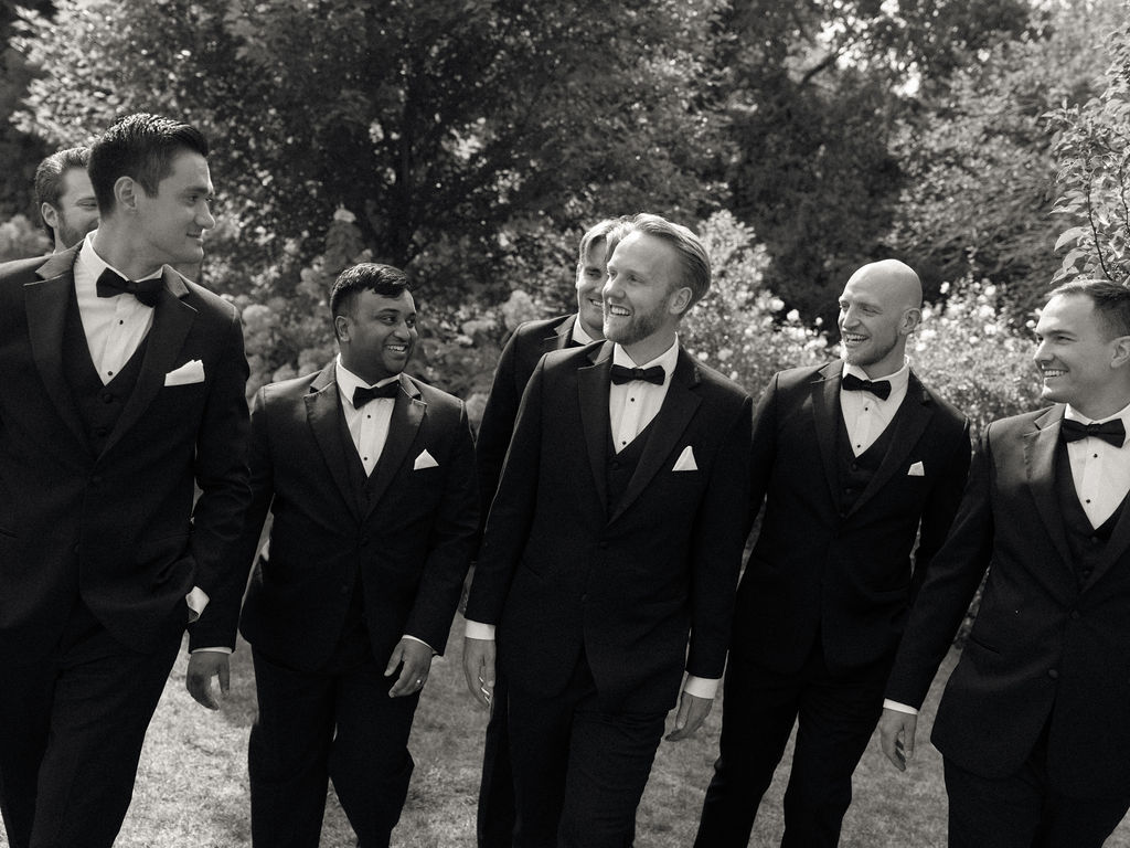Black and white photo of groomsmen walking and laughing during wedding party portraits.