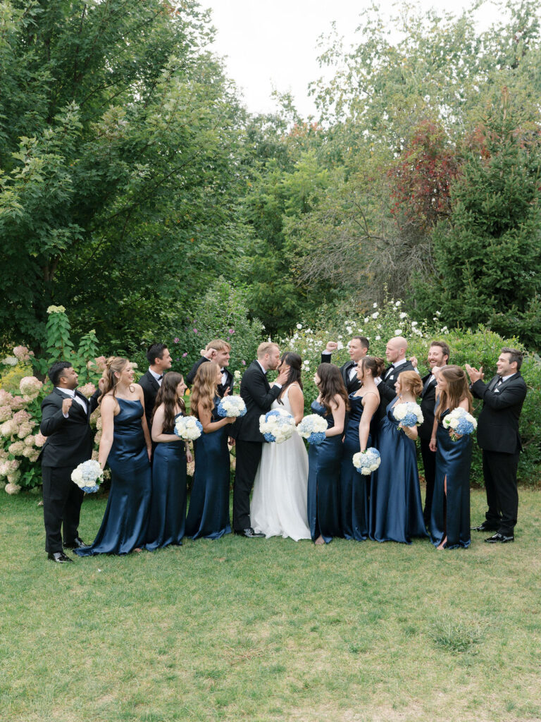Bride and groom surrounded by their wedding party during outdoor portraits at Bay Pointe Woods.