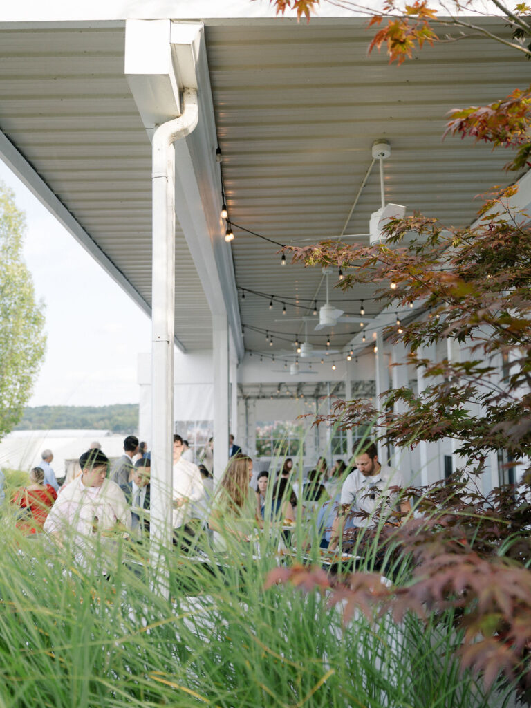 Candid moments of guests socializing beneath the pavilion at a lakeside wedding rehearsal.
