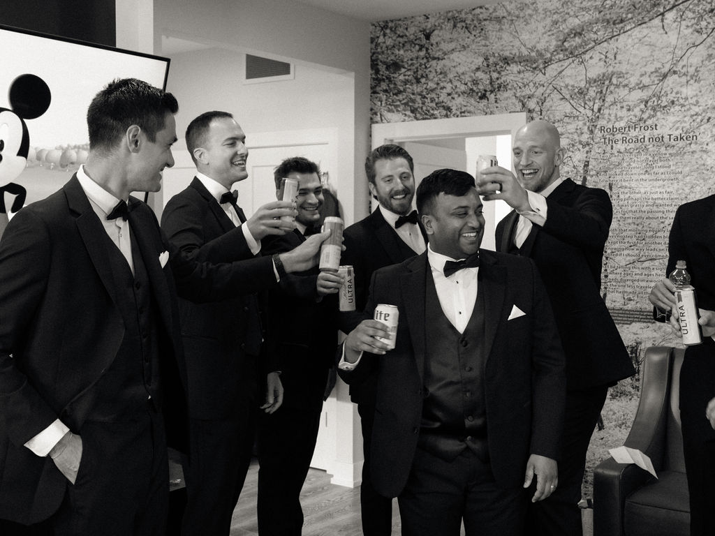 Black and white wide shot of a groom and his groomsmen having drinks.