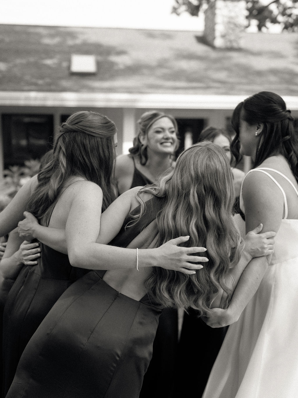 Black and white candid photo of a bride hugging her bridesmaids after their first look.