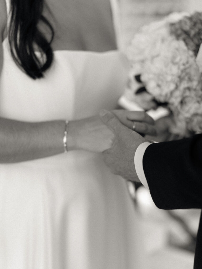 Black and white close up photo of a bride and groom holding hands during their first look.